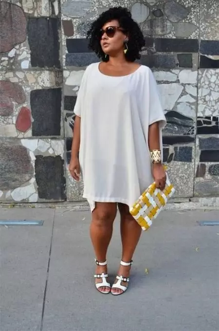 Biała sukienka tunikowa dla pełnych kobiet w połączeniu z białymi sandałami i akcesoriami złotymi