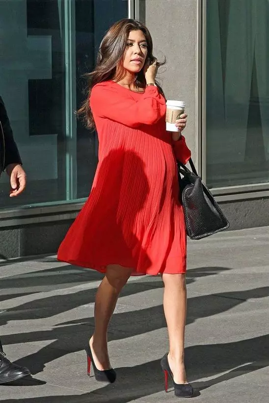 Röd klänning av lösa croes för gravida kvinnor i en kombination med svarta skor och svart väska