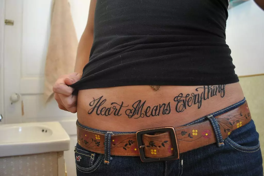 Tattoo në stomak (50 foto): Në kërthizë, në shtyp dhe bark në fund. Skica e tatuazheve të bukura. Shifrat e tatuazheve 1999 dhe 2002, 1998 dhe të tjerët, opsione të tjera për imazhe të vogla dhe të mëdha 13790_15